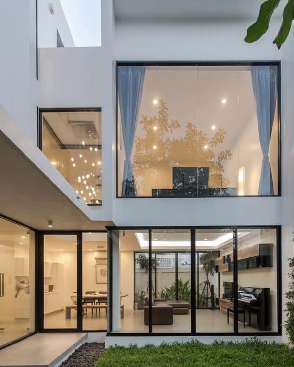 Two-storey home with full-height aluminium-framed glazing lit warmly from inside