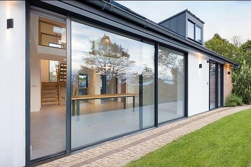 Aluminium sliding doors along the rear elevation of a house opening onto a lawn