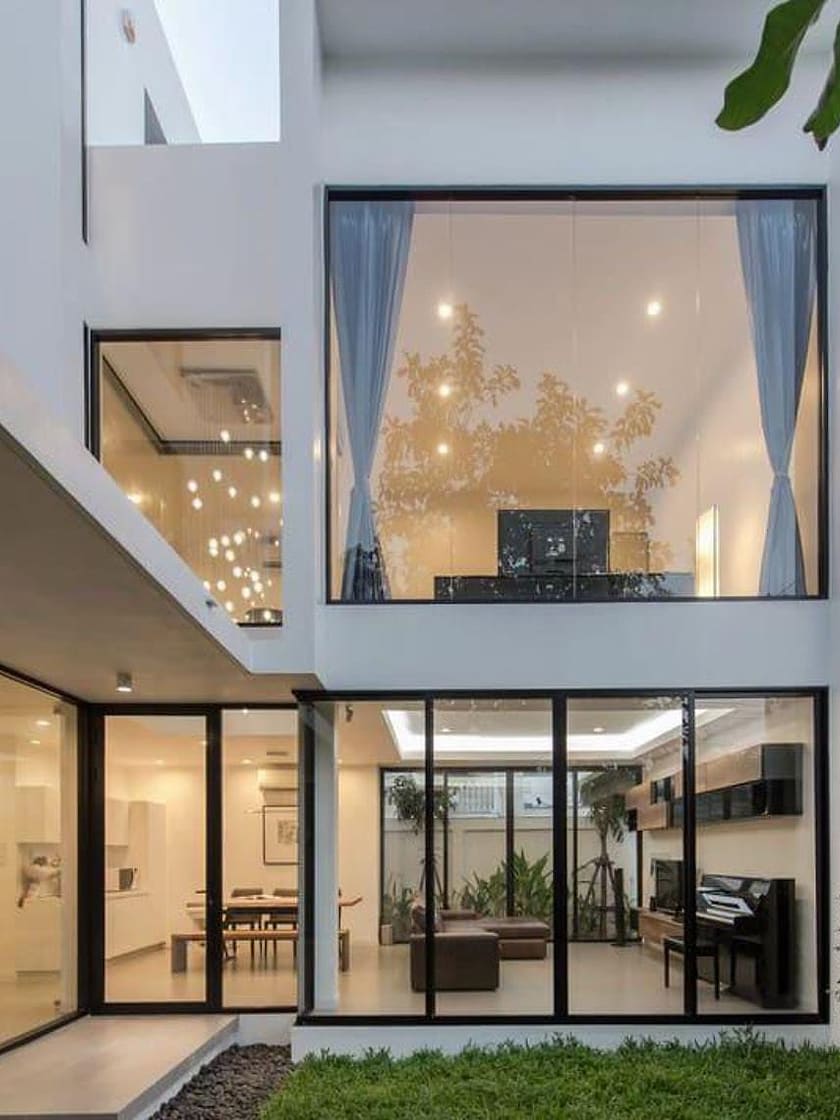 Two-storey home with large aluminium-framed glass windows lit warmly from inside